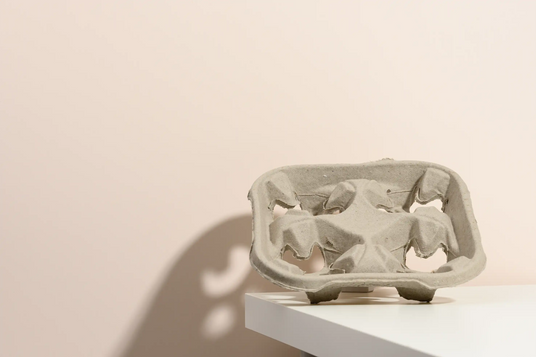 Tragetablett aus grauem Papier für 4 Becher auf weißer Tischkante vor beigem Hintergrund.